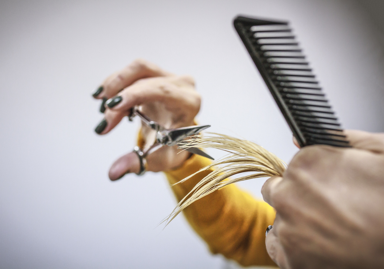Hairdresser holds scissors and comb in his hand and cuts the ends of hair. Copy space
